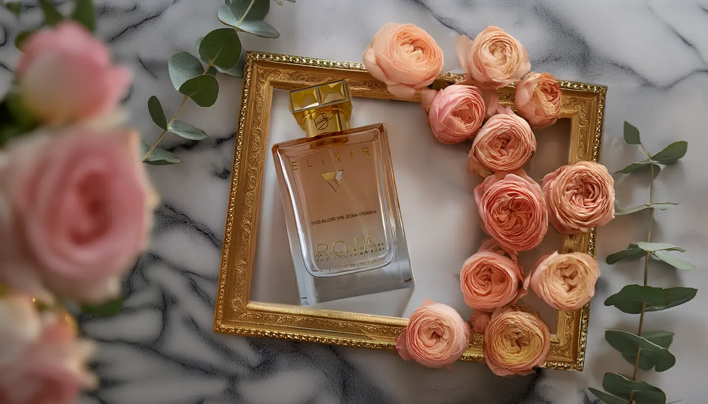 Roja Elixir Pour Femme displayed in a golden frame surrounded by pastel pink roses